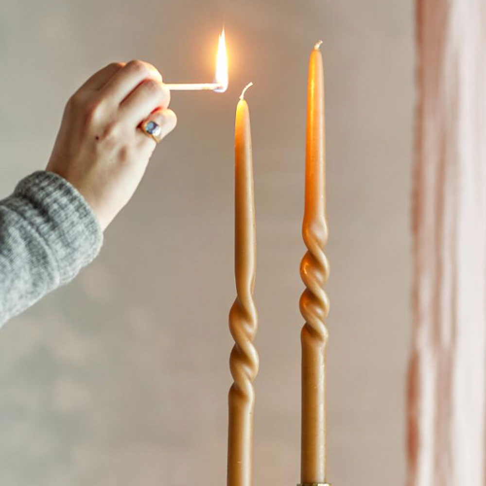 Person lighting a pair of Twist Dinner Candles in Caramel with a match