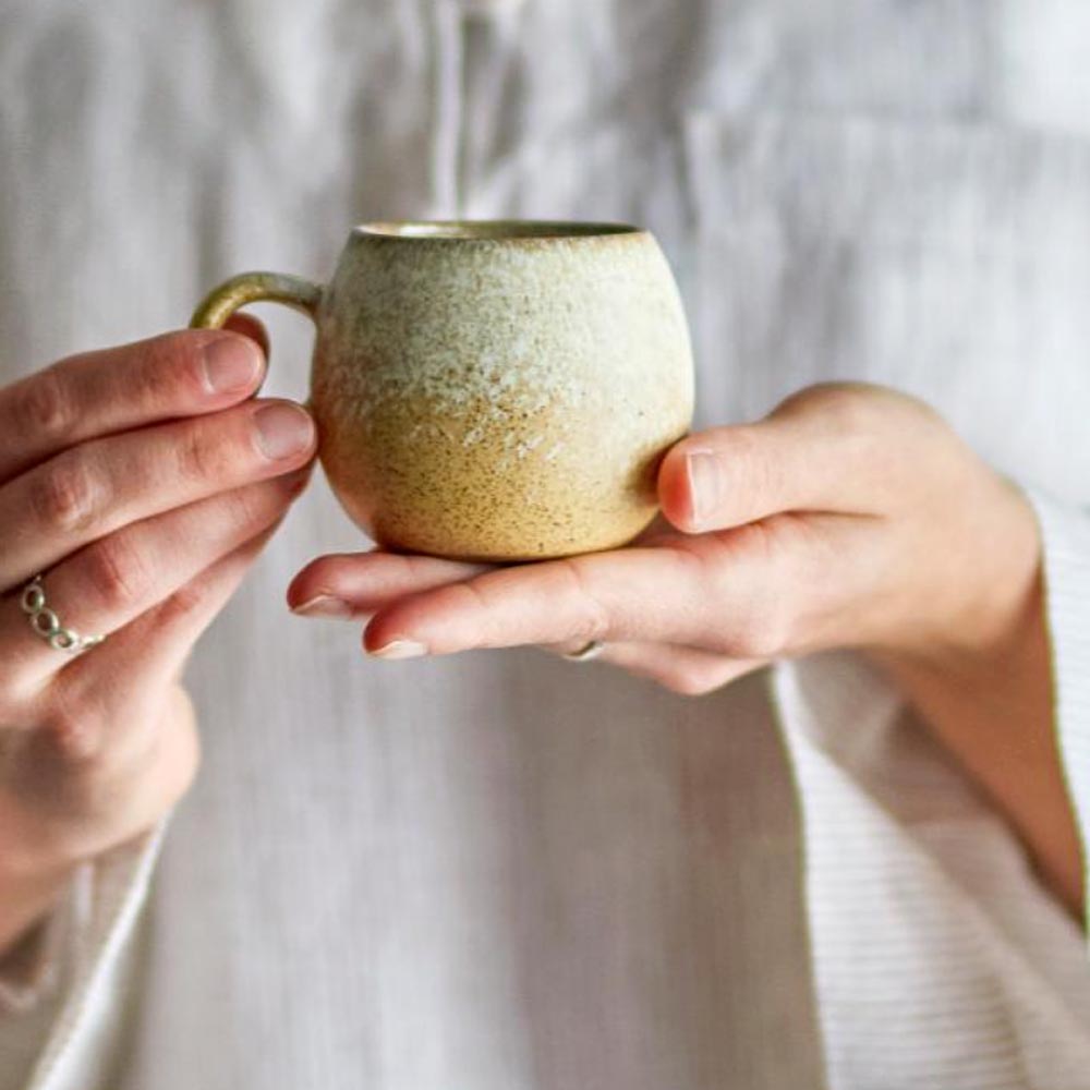 Paula Stoneware Espresso Cup in natural golden glaze, featuring a small round design and a comfortable handle, held in hand for a cosy coffee moment.