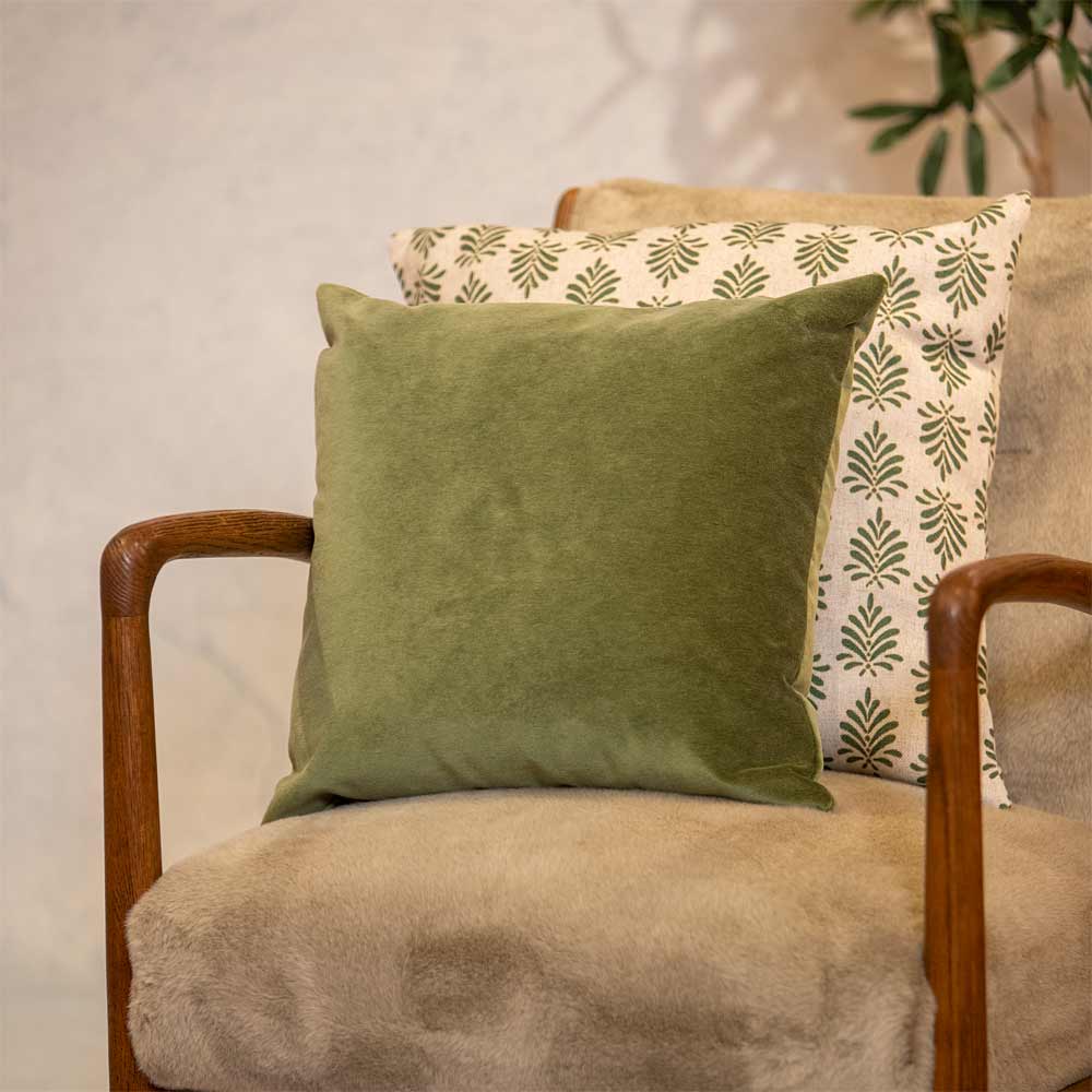 Green pillow on a beige armchair with a patterned green and white pillow in the background.