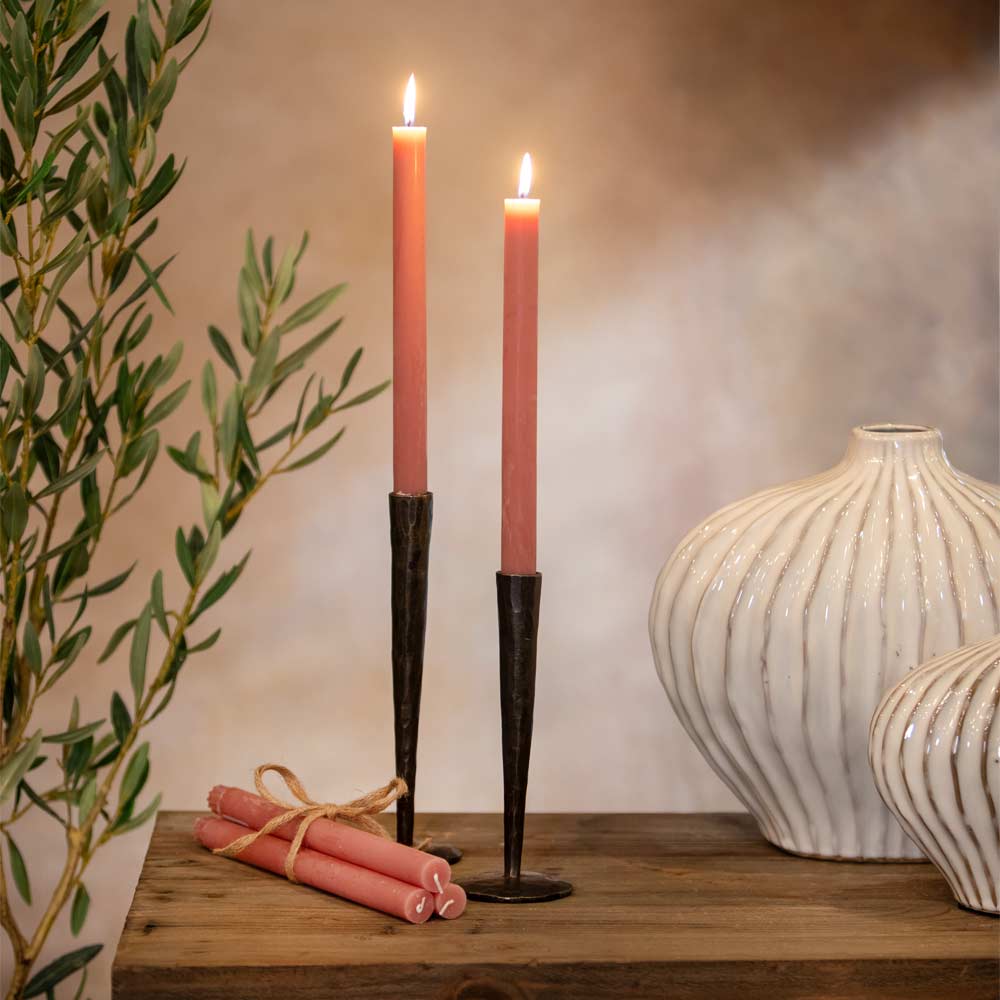Two Rustic pink candles in black holders on a wooden surface with decorative vases and a plant.