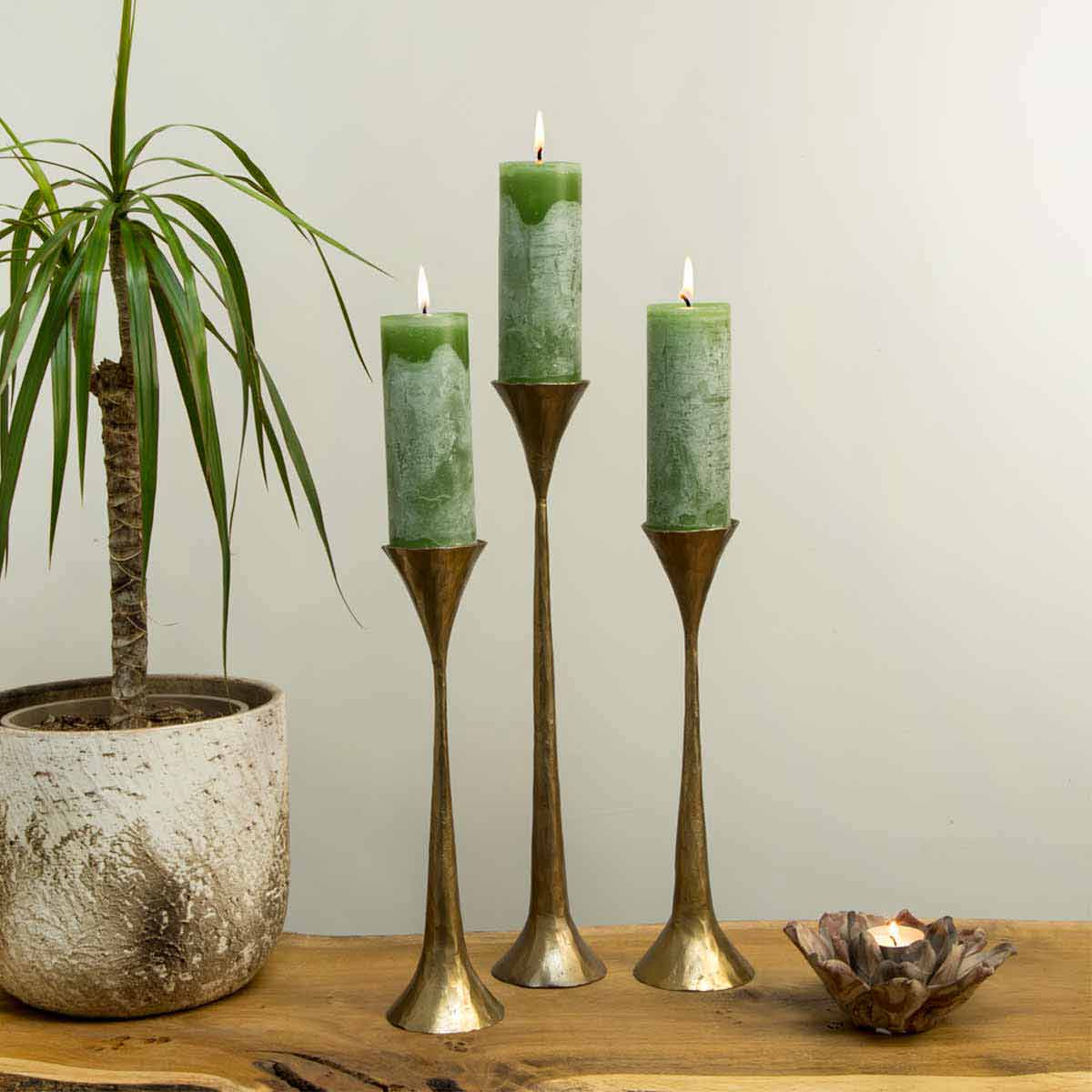 Rustic leaf green pillar candles in bronze holders on wood surface with potted plant – available in two heights.