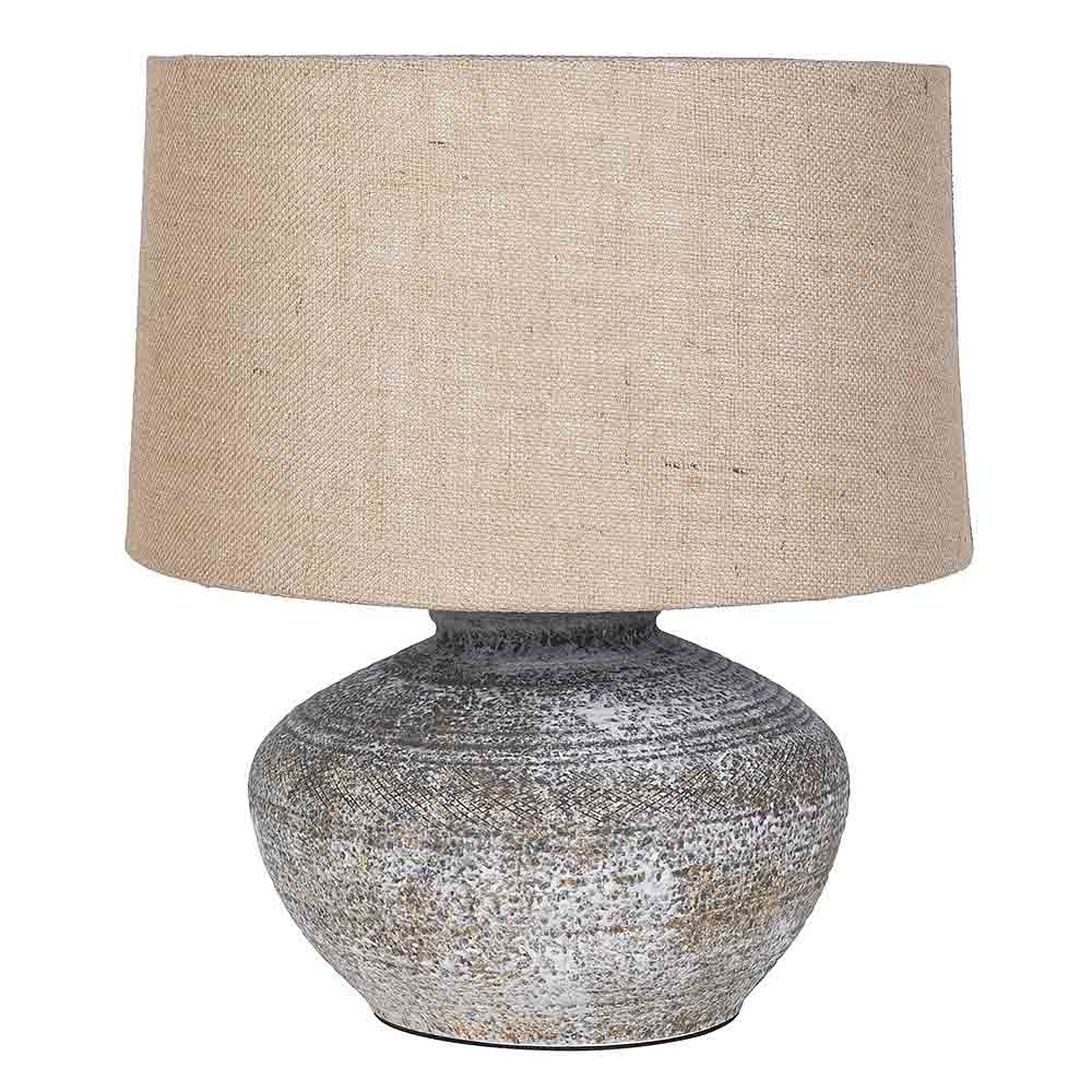 A table lamp with a textured, silver-gray and brown ceramic base and a large, tapered beige linen drum shade, shown against a plain white background.