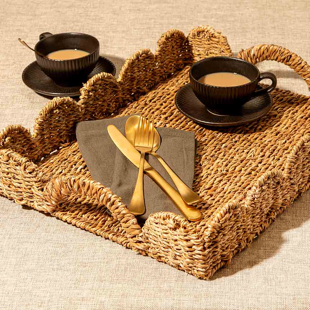 Café setting with cups, saucers, and gold cutlery on a woven tray.