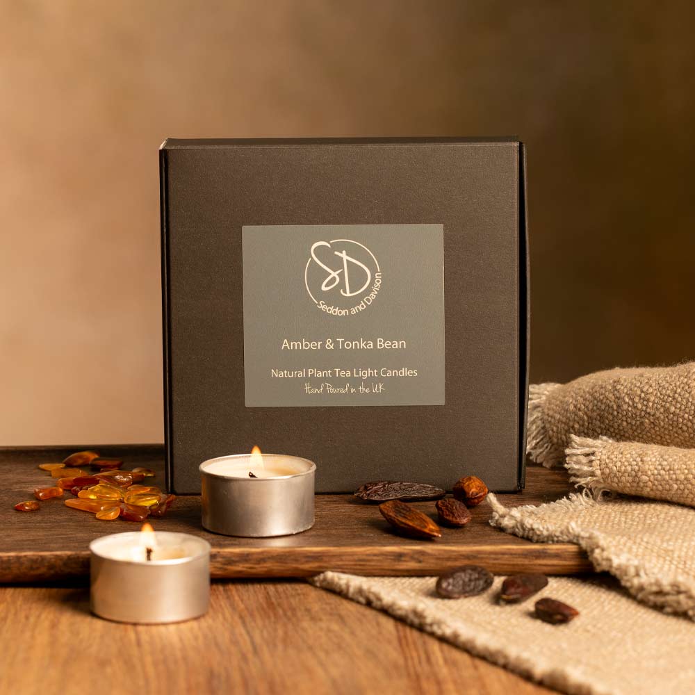 Amber and Tonka Bean candles with a branded box on a wooden surface