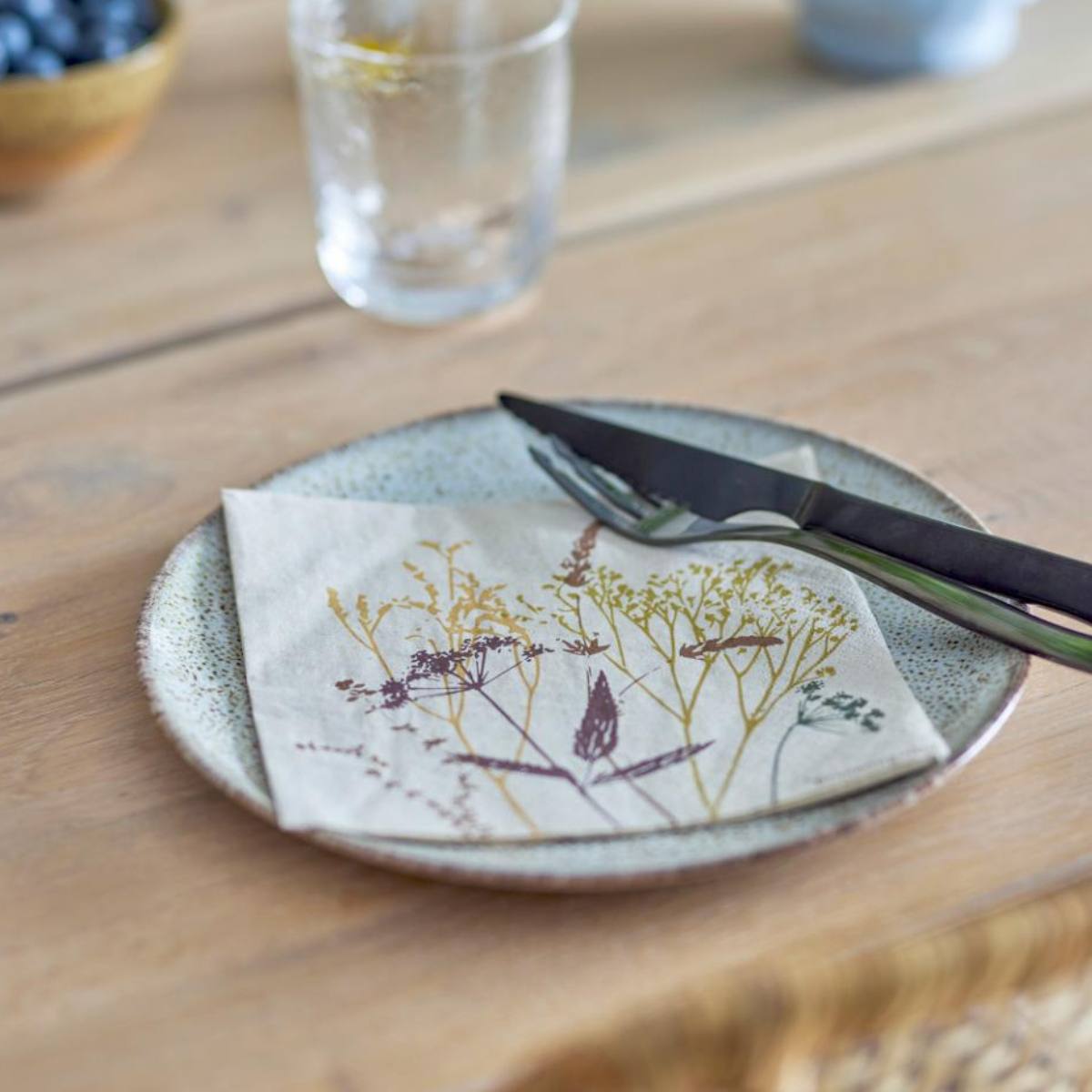 Ceramic plate with Sirri floral design napkin, and knife on a modern rustic wooden table.