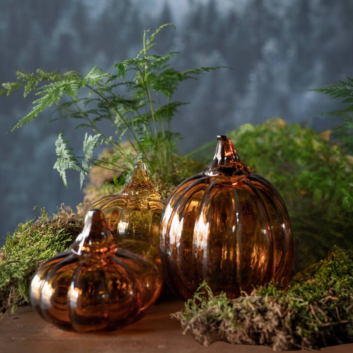 Three amber glass pumpkins on a bed of moss with a blurred natural background - Show Light and Dark Small Pumpkins