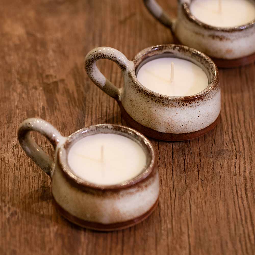 Three ceramic candle holders with candles on a wooden surface