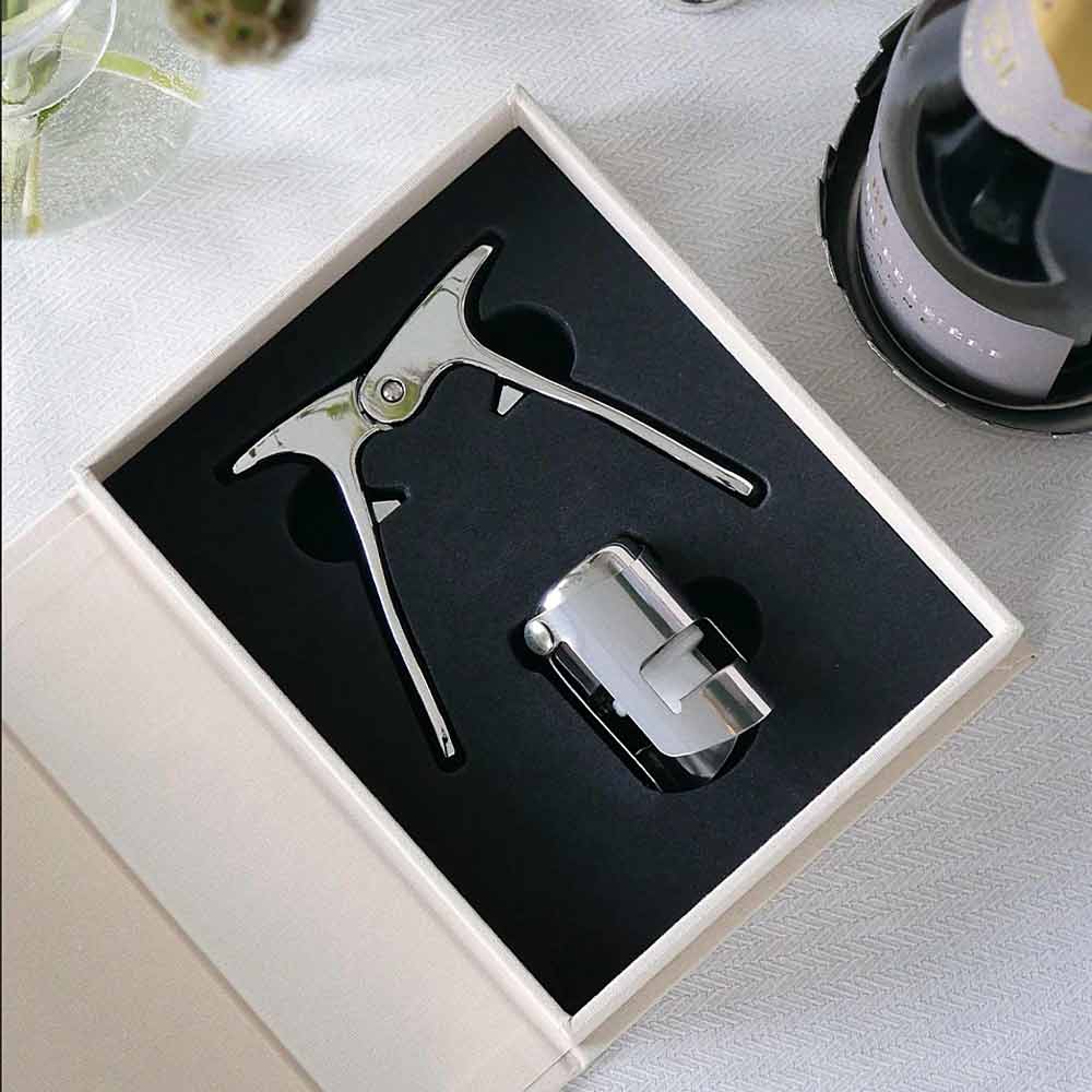 Silver bottle opener and cap catcher set in a box on a table with a bottle in the background - part of The Essentials - Champagne Tools Gift Set