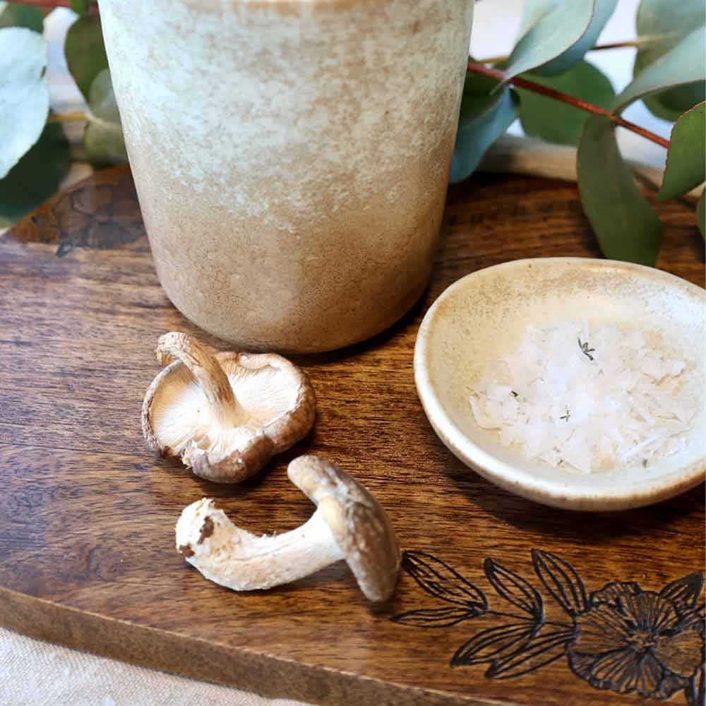 Two mushrooms on the Tours Wooden Tapas Board with Flower Carving with a small bowl of salt and a ceramic container.