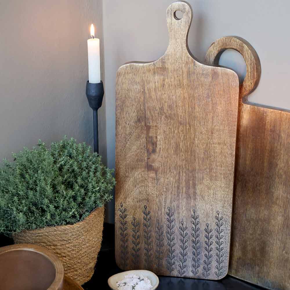 Tours Wooden Tapas Board with leaf patterns on a surface with a candle and plant in the background.