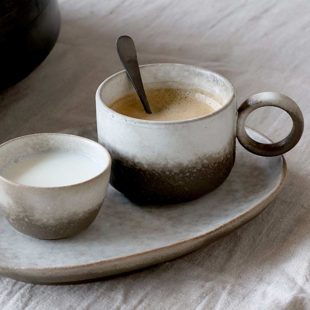 Ceramic mug with a spoon, small bowl, and saucer on a ceramic tray
