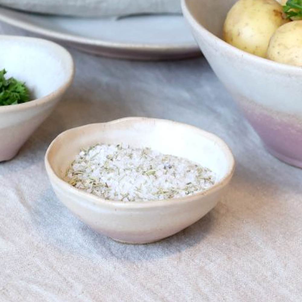 Valence Small Bowl in Dusty Rose with salt on a table with other bowls and food in the background