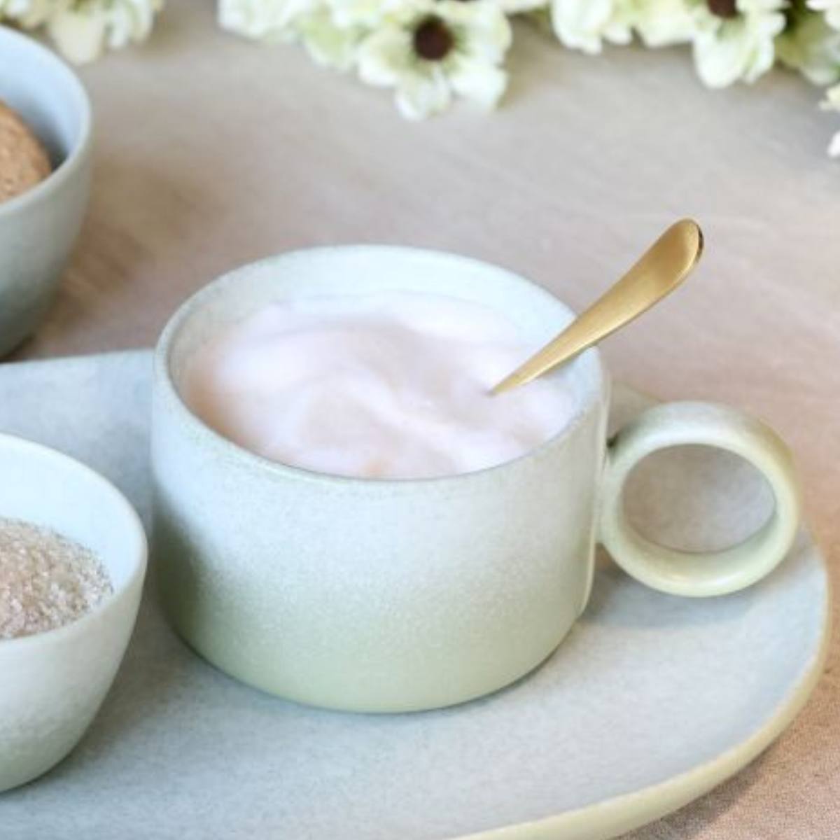 Light green Valence Porcelain mug in Verte Green with a spoon on plate, surrounded by small bowls and flowers.