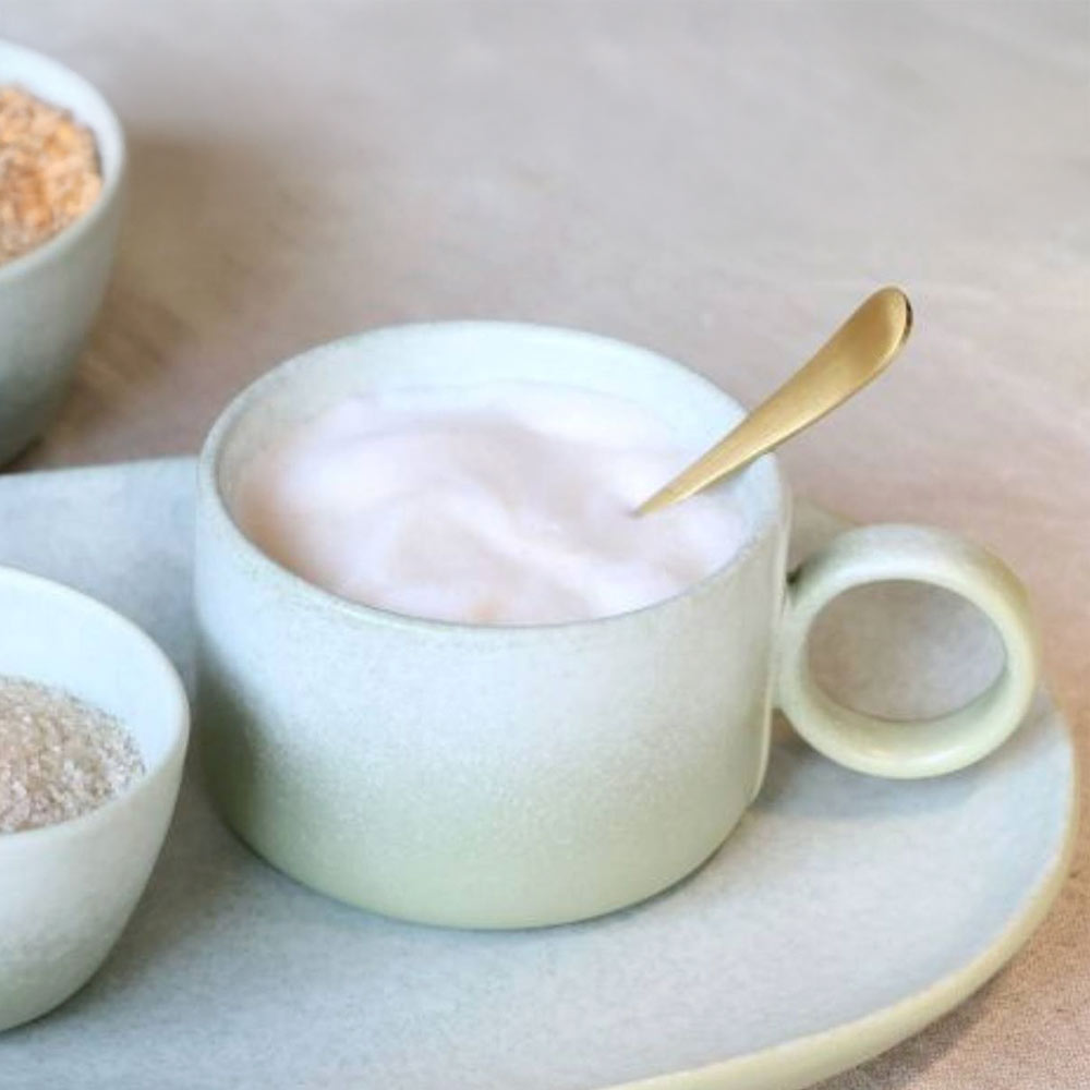 Light green Valence Porcelain mug in Verte Green with a spoon on plate, surrounded by small bowls and flowers.