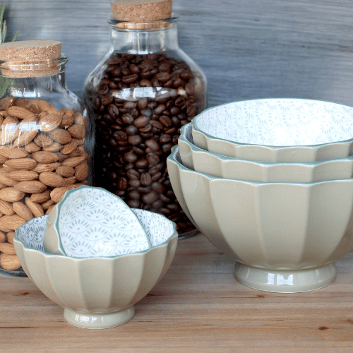 Ares set of 5 porcelain bowls in Verte (green) with a fluted design and patterned interior, displayed on a wooden surface with glass jars filled with coffee beans and almonds in the background.