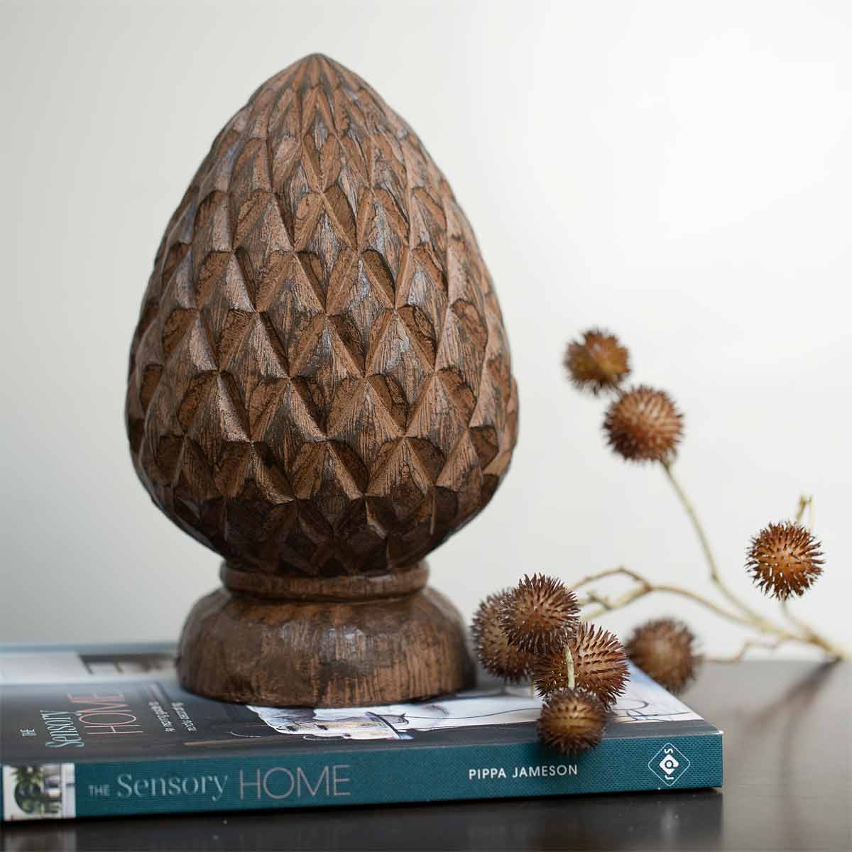 Wood effect artichoke sculpture with carved texture and warm brown finish displayed on a book