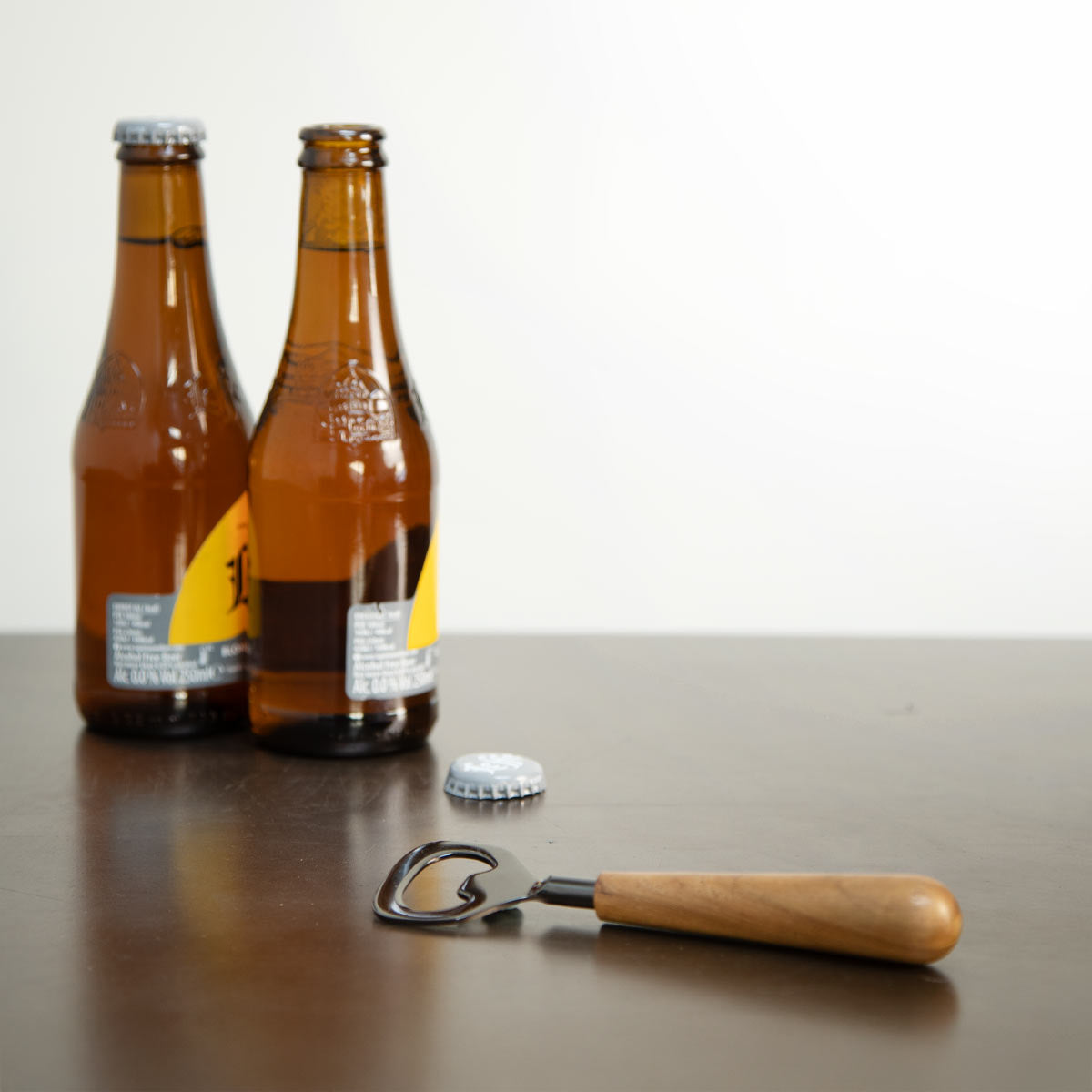 Onyx and wood bottle opener with smooth wooden handle, displayed on a kitchen counter beside beer bottles.