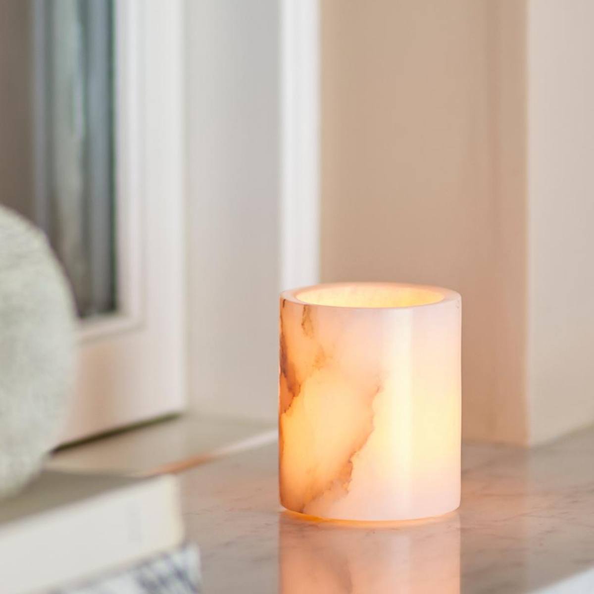 Annabel white alabaster tealight holder with natural veining and polished finish styled on marble top - showing candle alight