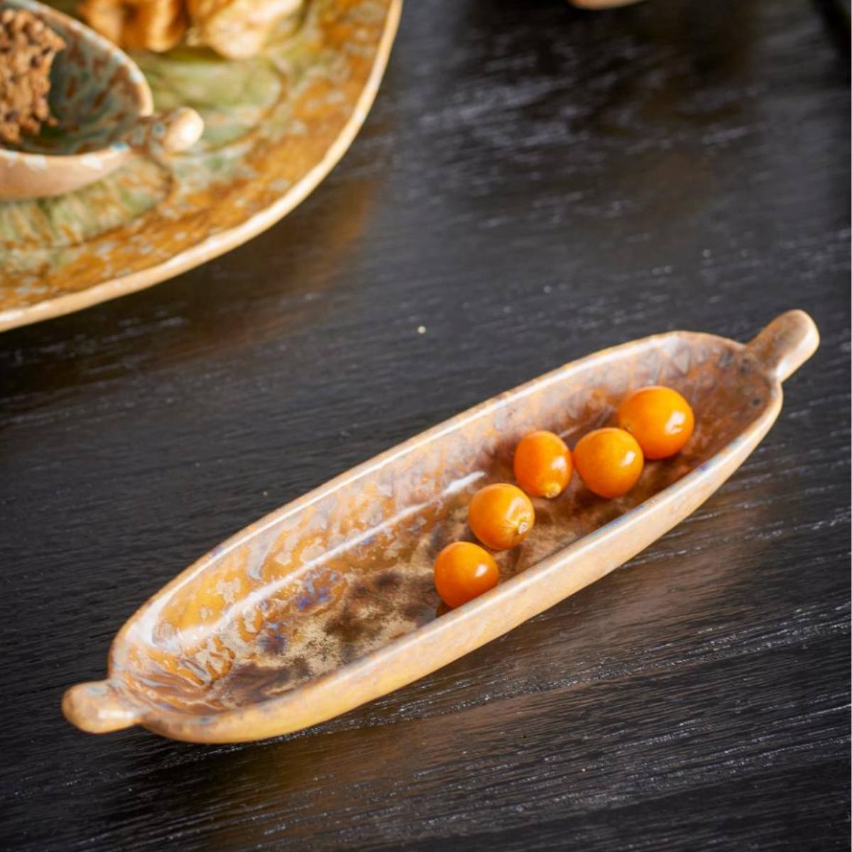 Milani ochre stoneware shallow dish with reactive glaze, displayed with small orange fruits on a dark surface