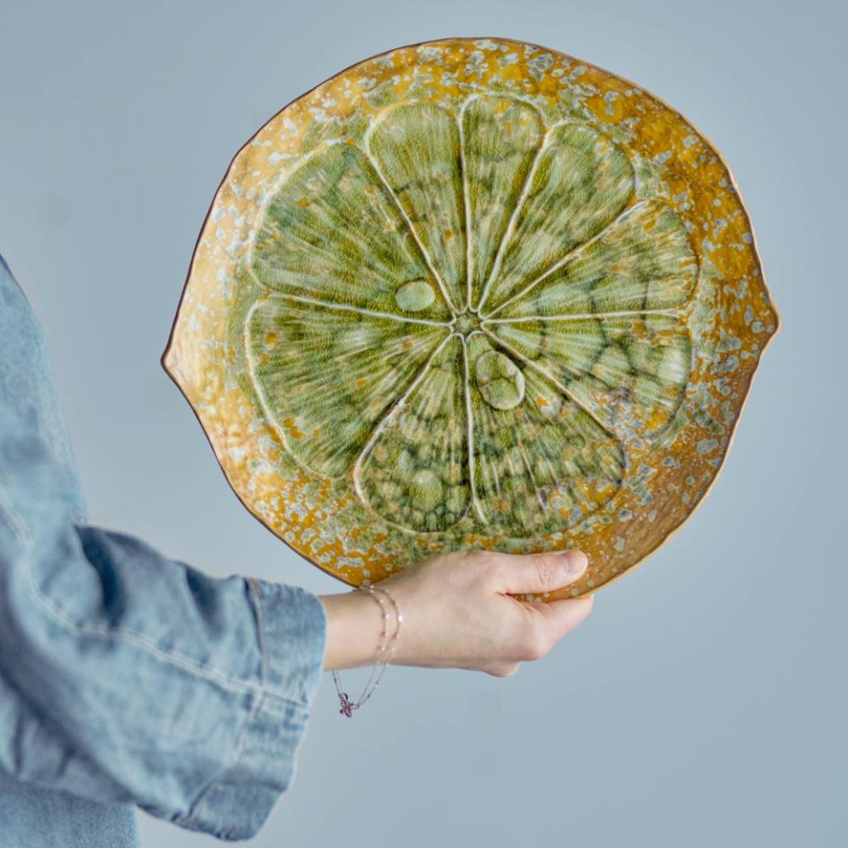 Milani Stoneware Serving Plate in Green - Person holding a round ceramic plate with green citrus design against a light blue background
