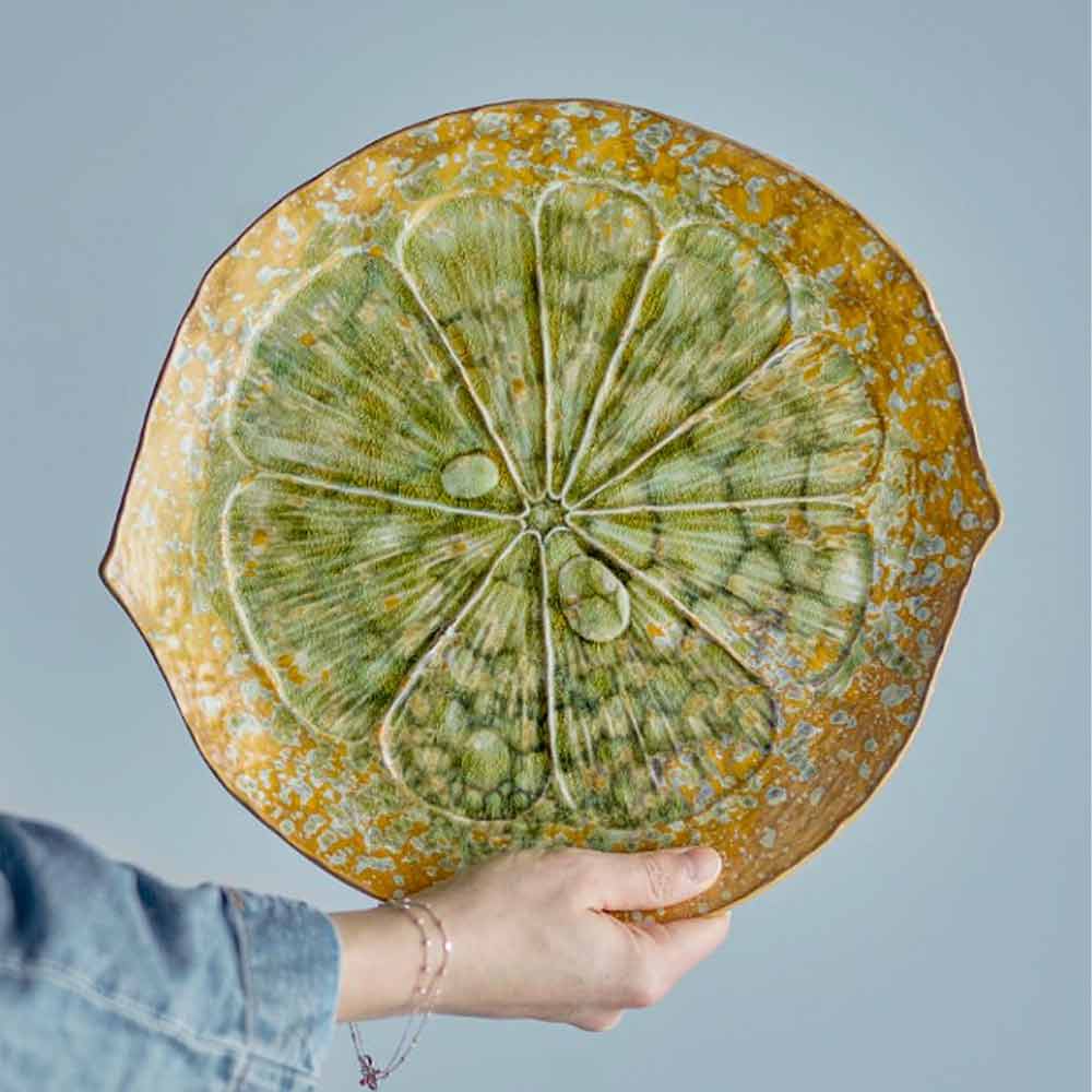 Milani Stoneware Serving Plate in Green - Person holding a round ceramic plate with green citrus design against a light blue background