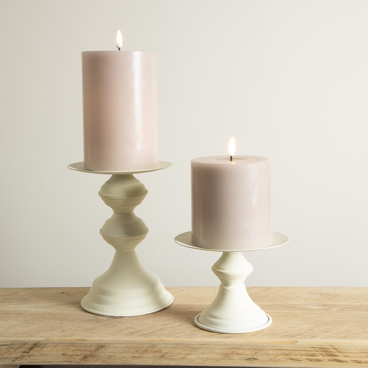 Tall and short pale rose LED pillar candles on sculptural white candleholders