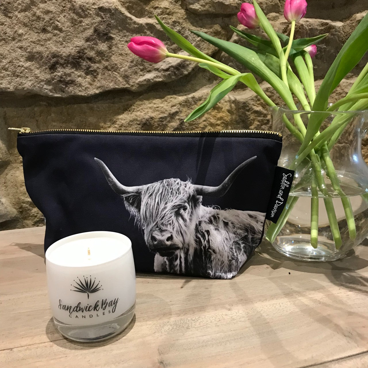Highland cow washbag in navy displayed with sandwick bay candle and pink flowers in a jar