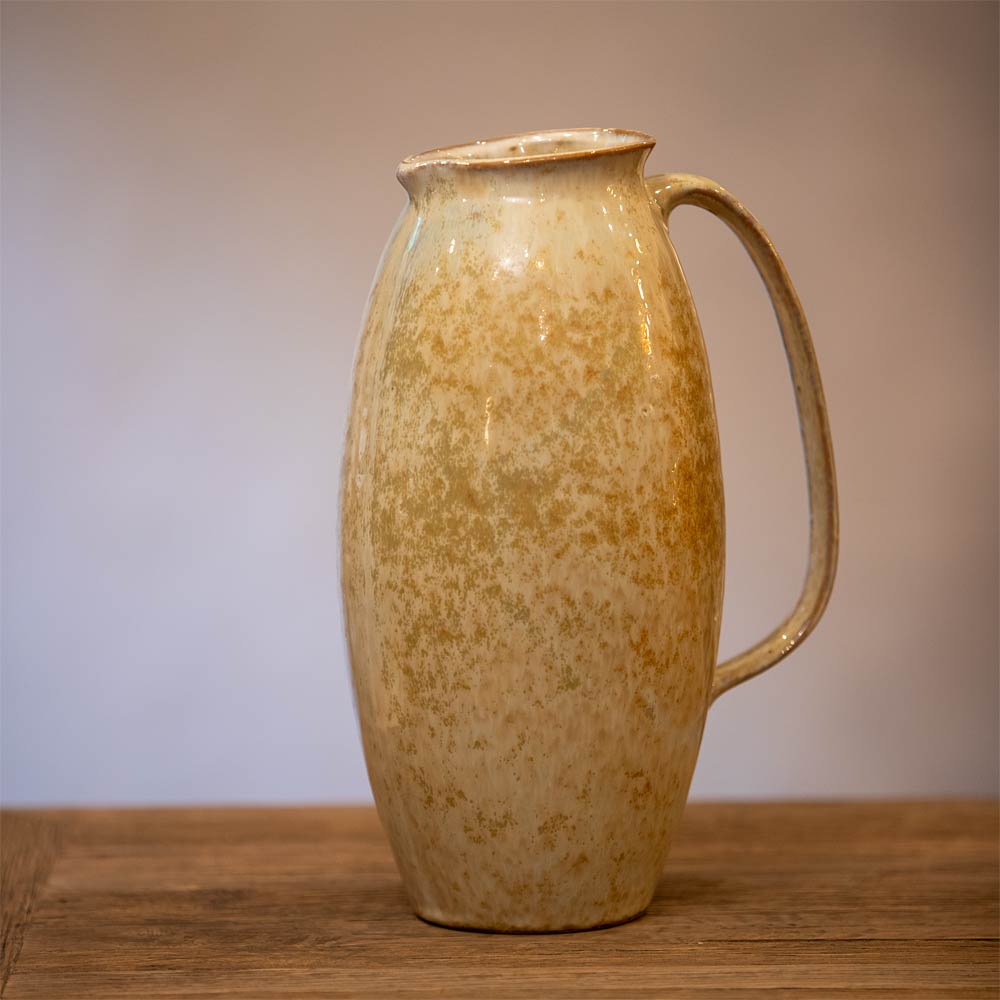 Ceramic pitcher with a handle on a wooden surface and gradient background