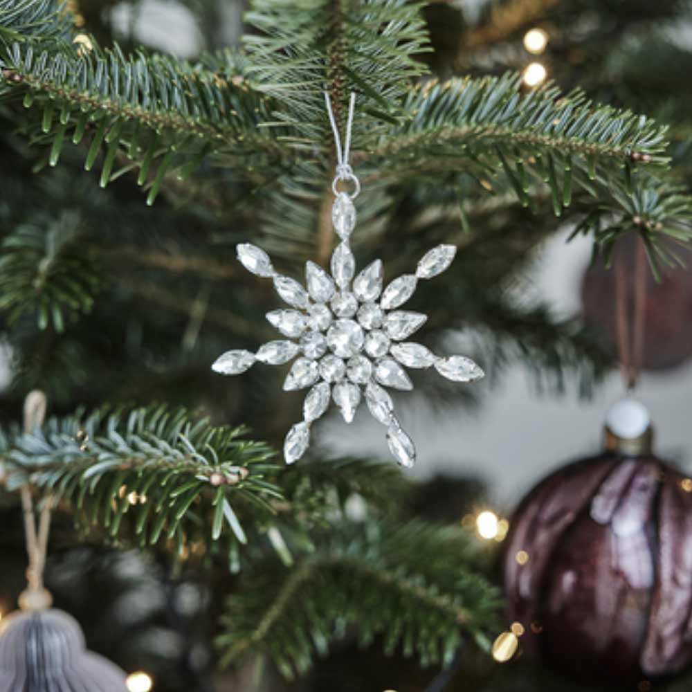 Decorative Ada Festive Silver Glass Tree Snowflake Tree Ornament with clear gemstones on a Christmas tree with blurred lights in the background