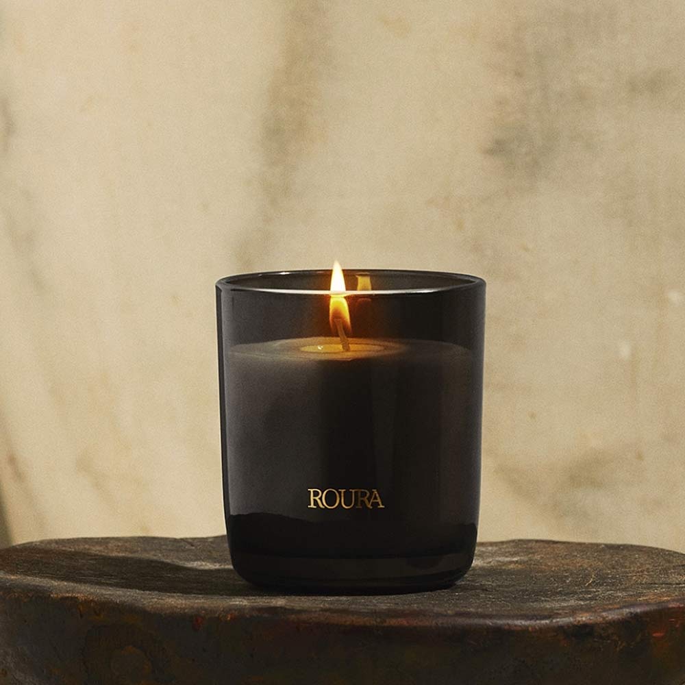 Ancient Woods Black Glass Jar Candle by Roura on a wooden surface against a beige background