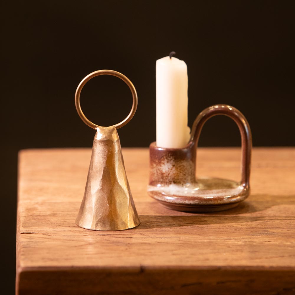 Brass bell candle snuffer and ceramic candle holder with candle on a wooden surface