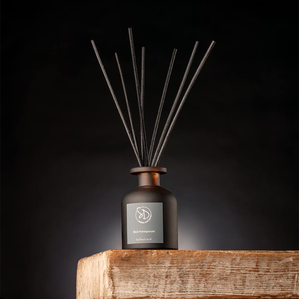 Black Pomegranate Reed diffuser with a dark amber bottle on a wooden surface against a black background