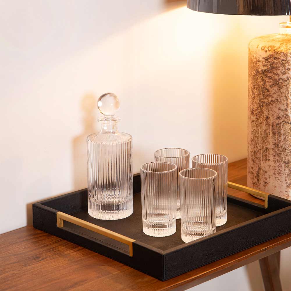 Set of glass decanter and tumblers on a Black Faux Shagreen Tray with Gold Handles with a lamp in the background.