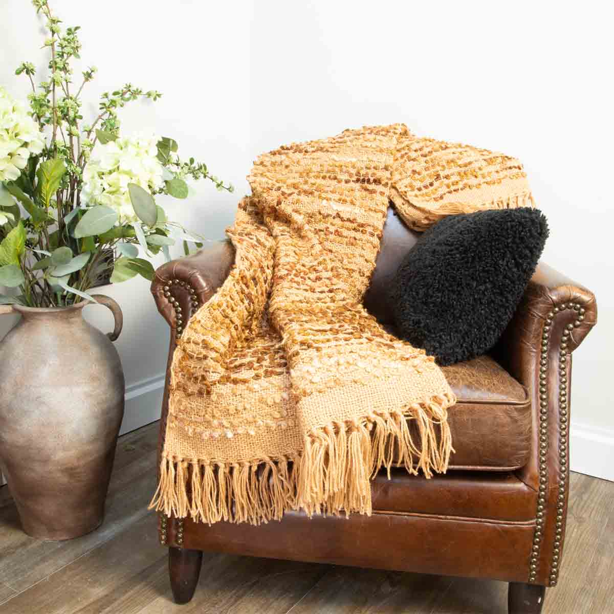 Cazar Throw in brown draped over a leather armchair, styled with a black Faux Fur cushion, drenched in early morning light.