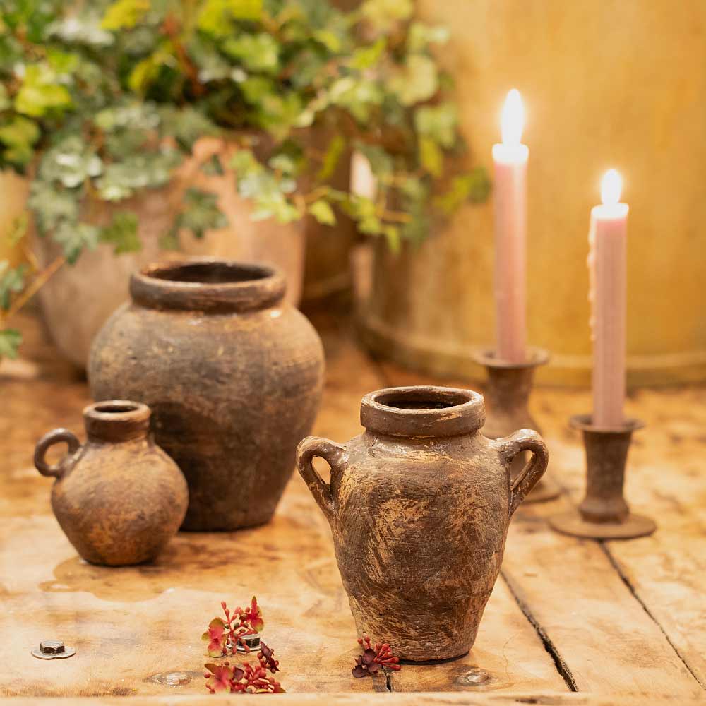 Vintage style Daiane Brown Terracotta Vases and lit candles on a wooden surface with plants in the background
