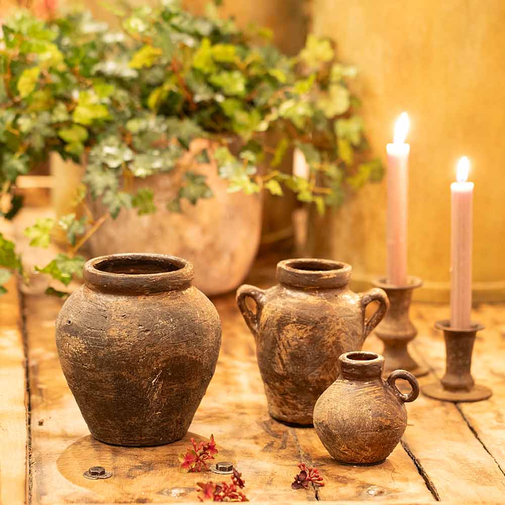 Vintage style Daiane Brown Terracotta Vases and lit candles on a wooden surface with plants in the background