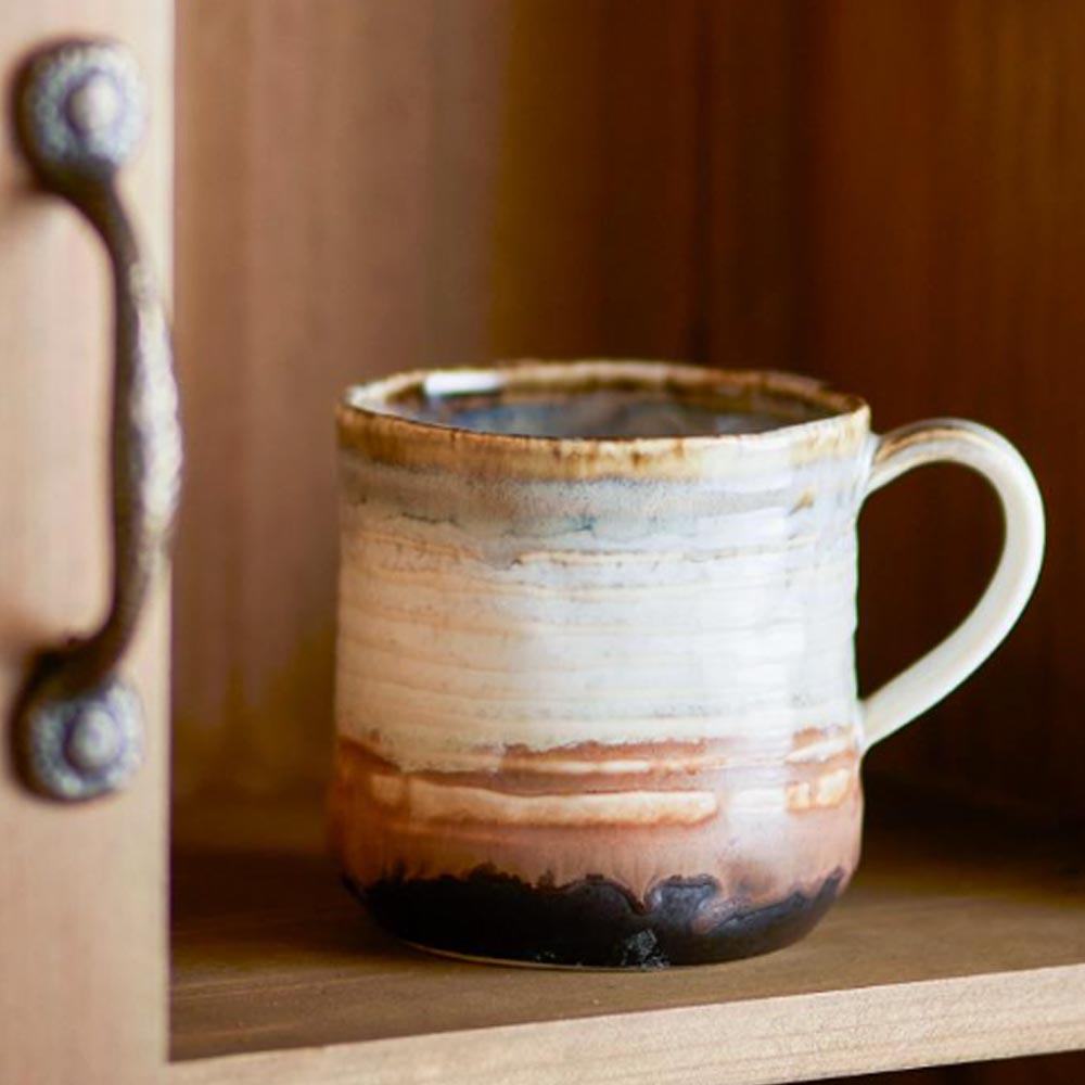 Ceramic Deana mug with brown and white glaze on a wooden shelf