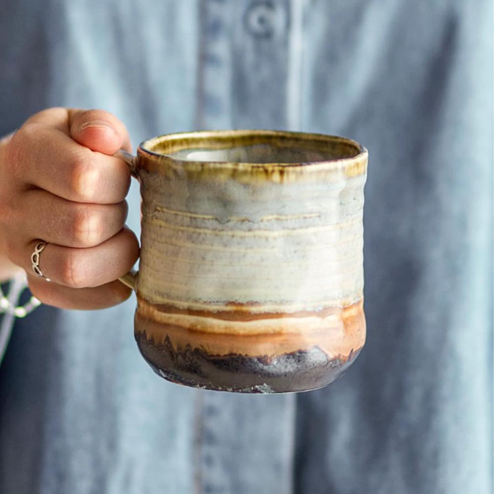 Hand holding a ceramic mug with a textured surface against a blurred background