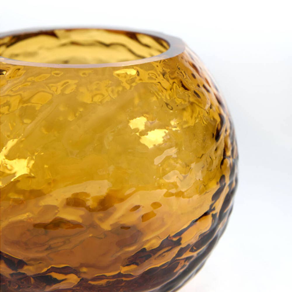 Close-up of a round amber glass candle holder with a hammered texture on a white background.