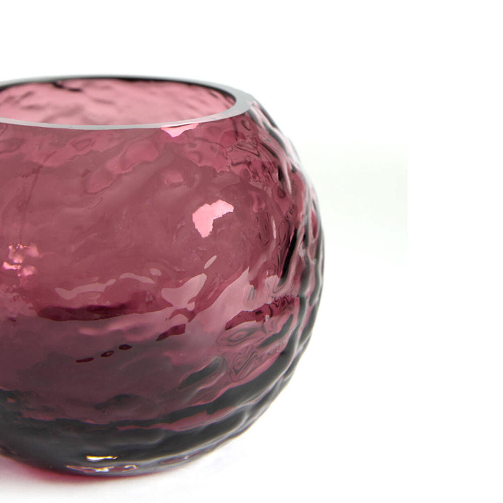 A close-up of a round, textured glass candle holder in plum colour, set against a plain white background.
