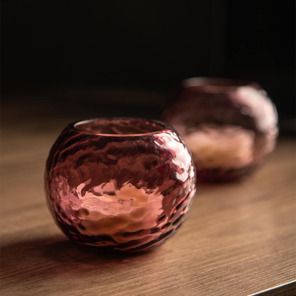 Two small hammered glass candle holders with a plum finish, displayed on a wooden surface with a dark background.