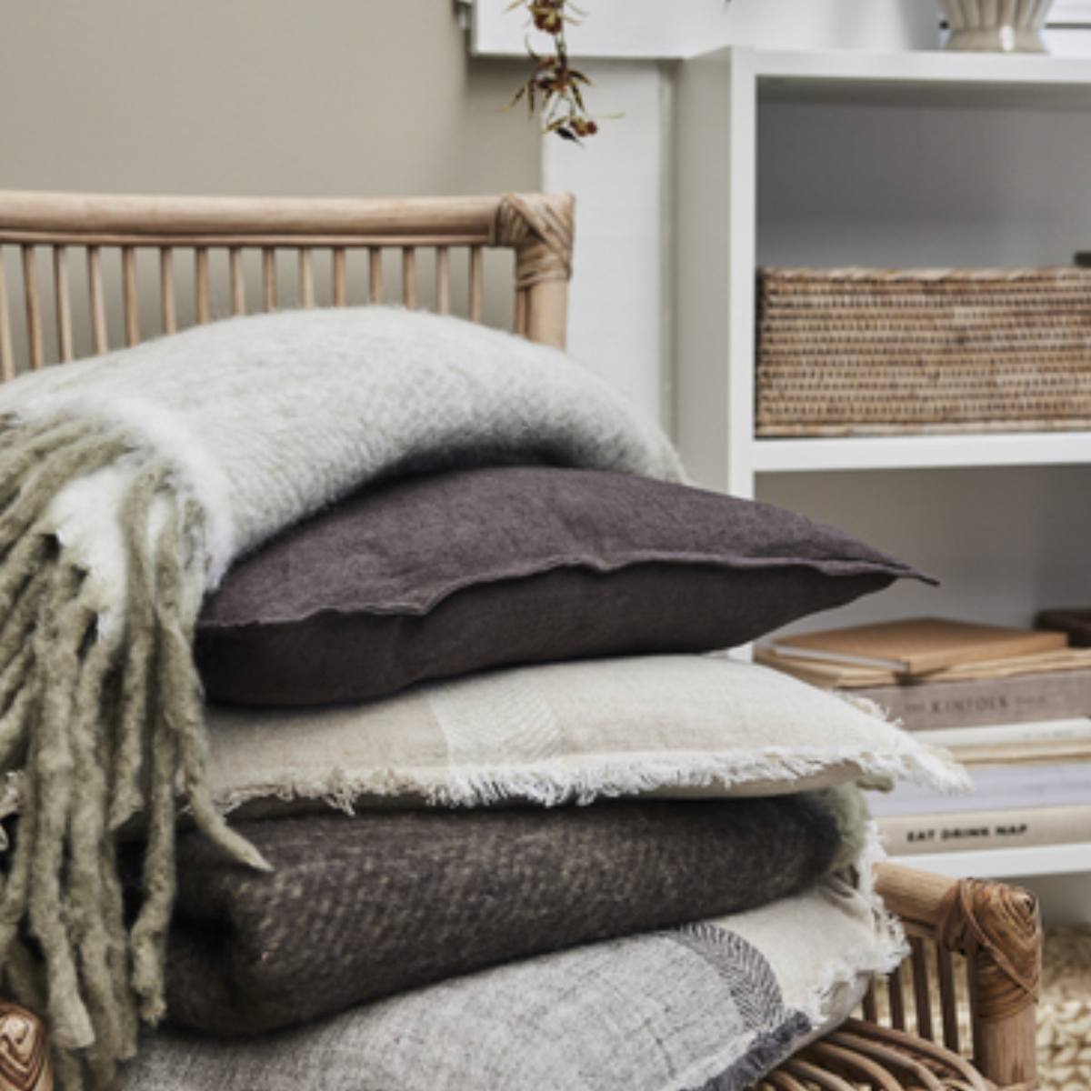 Stack of textured pillows and blankets on a wooden chair with a neutral background - Featuring the Efina Dark Brown Linen Oblong Cushion
