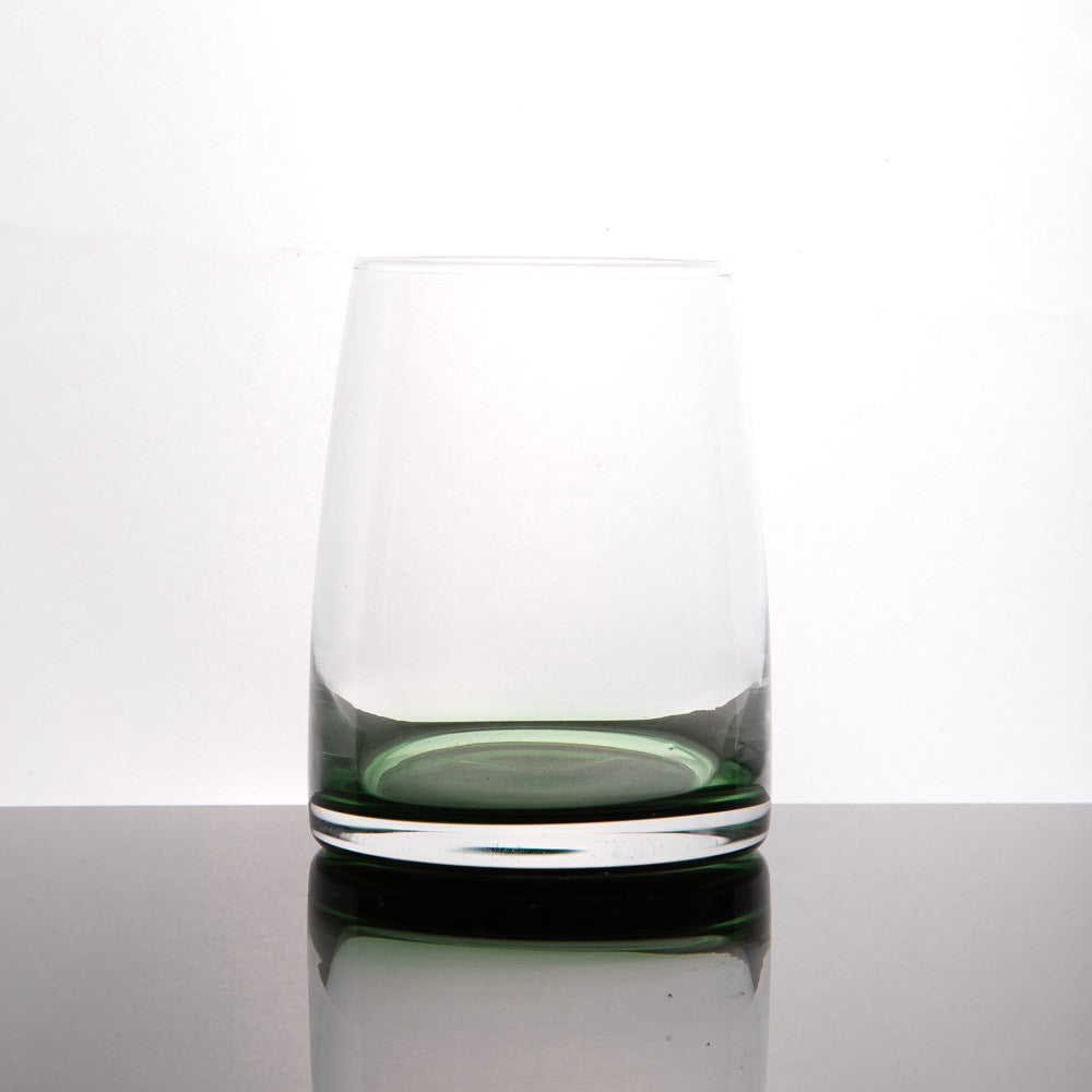 A clear glass tumbler with a dark green tinted base, shown on a reflective dark surface against a white  background.
