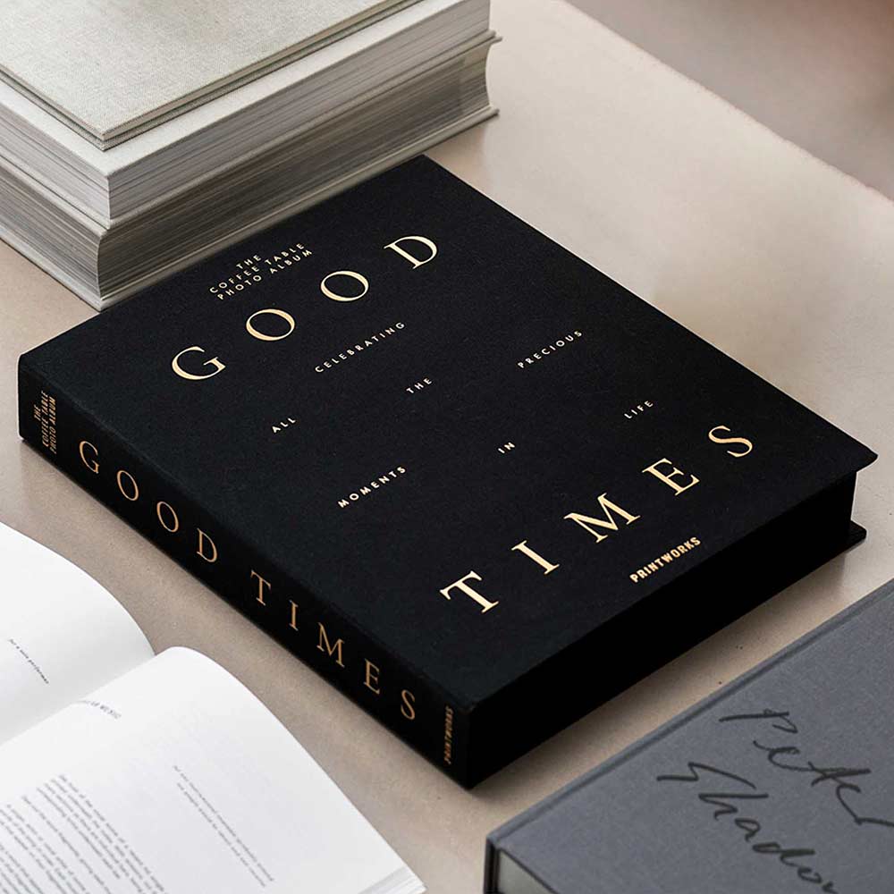 Black cloth photo album titled “Good Times” with gold lettering, styled on a desk with books.
