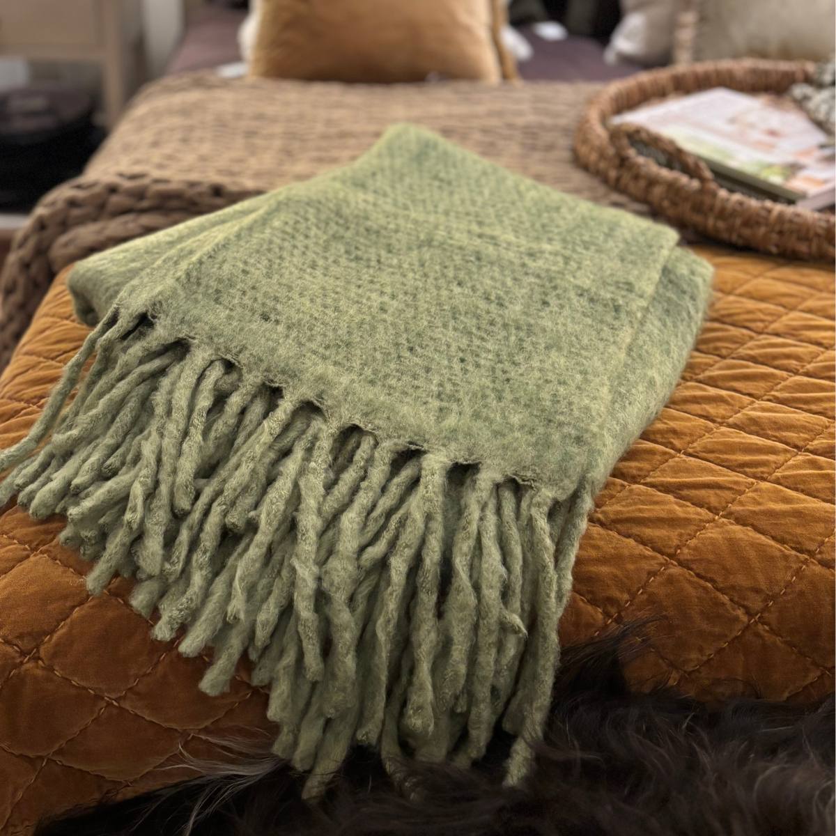 Guada Soft Green Woven Throw with Fringe displayed on bed with caramel bedspreads