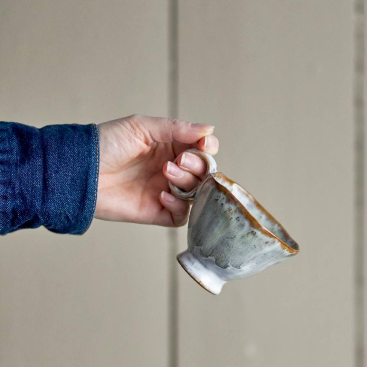 Hand holding a handmade Imogen cup with grey-green reactive glaze  with a neutral background