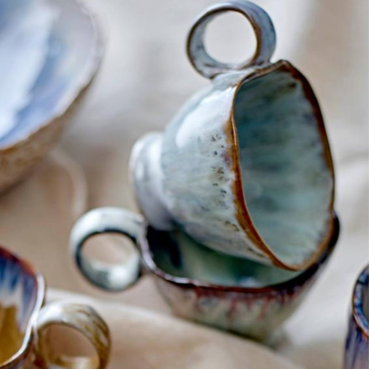 Handmade Imogen cup with grey-green reactive glaze stacked on other cups on a table