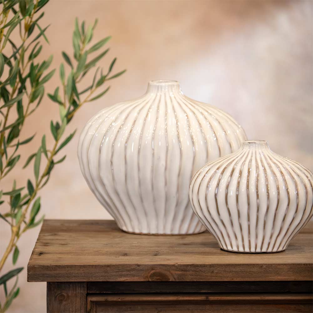 Two ribbed ceramic vases on a wooden table with a blurred background
