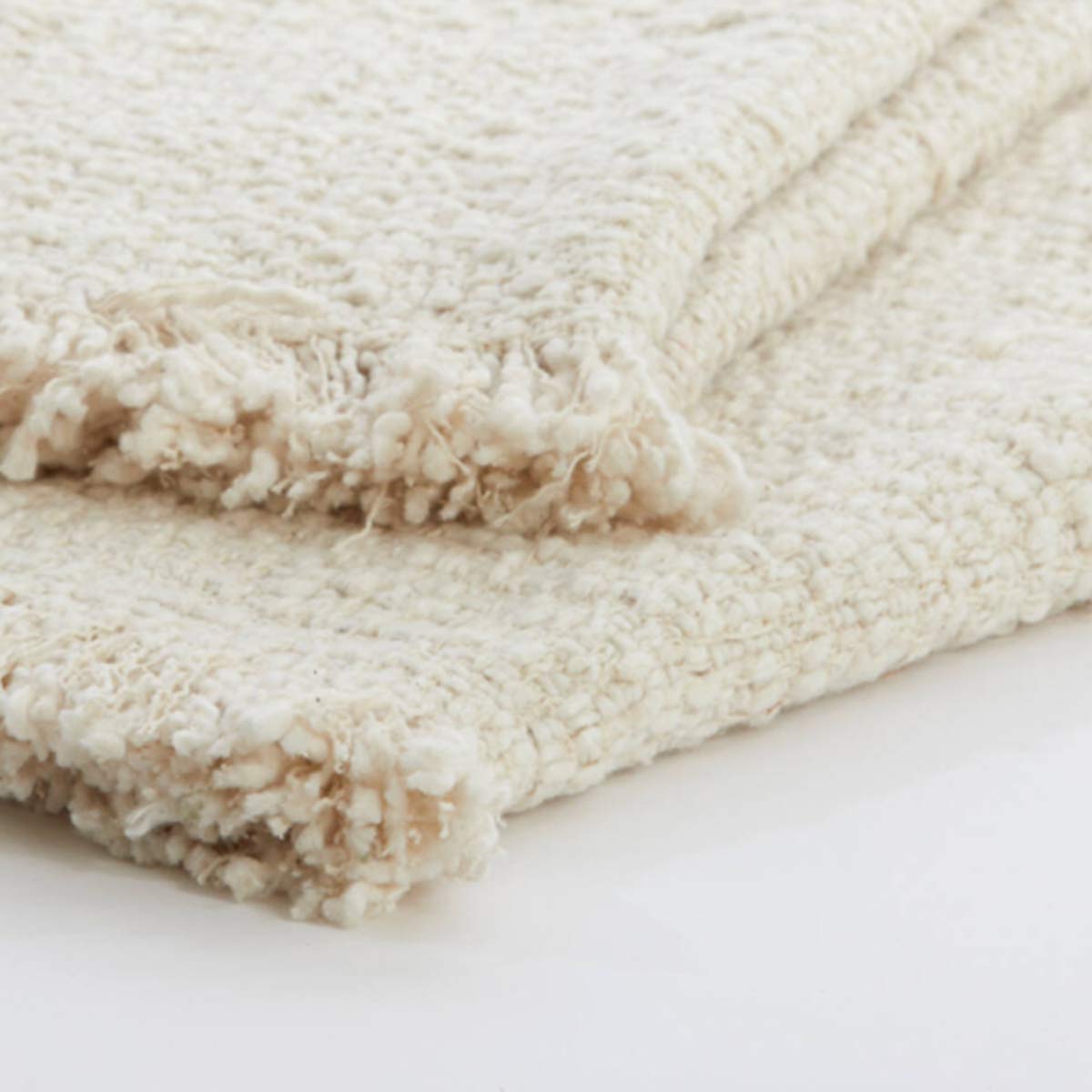 Close-up of the Miraso throw's woven texture, showing the intricate cotton weave and delicate fringed edges in a soft natural shade.