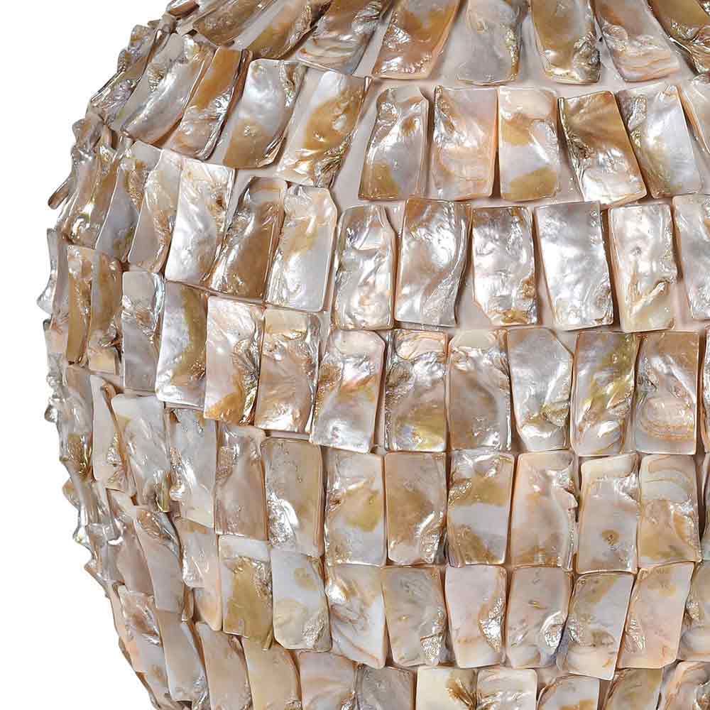 A close-up of a decorative spherical object covered in overlapping iridescent shell tiles in soft beige, cream, and pearly tones, shown against a plain white background.